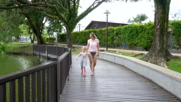 Mutlu anne ve kız şehir parkında göletin kenarında yürüyorlar. — Stok video