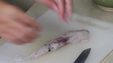 Ev hanımı mutfak masasında çiğ kalamar pişiriyor.