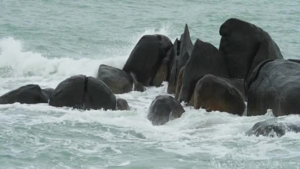 Golven breken af op donkere rotsen bij het strand — Stockvideo