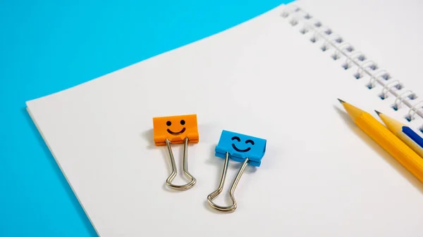 Orange Color and Blue Smile Binder Clips with Pencils on Notepad