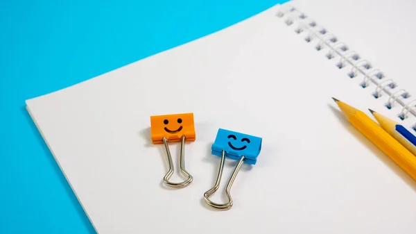 Oranje kleur en blauwe glimlach binder clips met potloden op notitieblok Rechtenvrije Stockfoto's