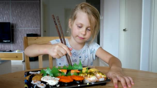 Симпатична дитина молода дівчина бере палички і їсть японські варіації суші їжі — стокове відео