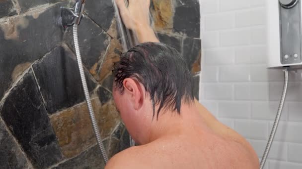 Onherkenbaar naakt brunette man leunend op muur het nemen van douche in badkamer — Stockvideo