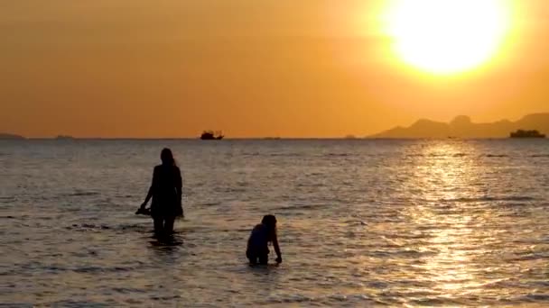 Silhouetten von Mutter und Tochter gehen bei dramatischem Sonnenuntergang auf Meerwasseroberfläche — Stockvideo