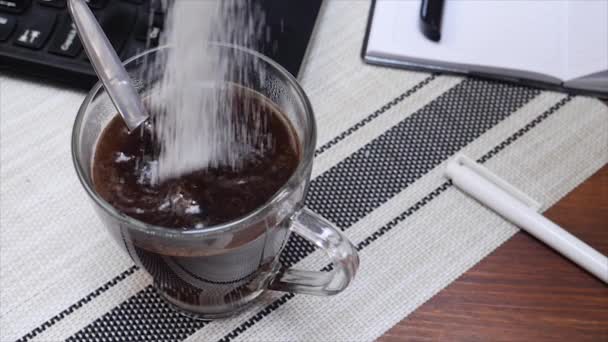 Azúcar blanco cae en la taza de café en la mesa de trabajo con el ordenador portátil — Vídeos de Stock