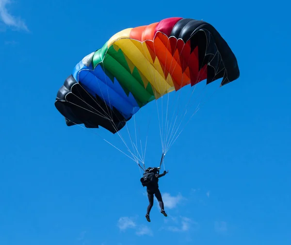 Skydiver з дуже яскравим барвистим парашутом на спині блакитного неба Ліцензійні Стокові Зображення