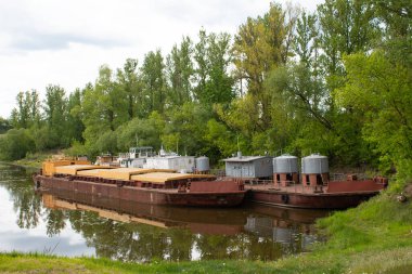 Nehir taşıması. Bir çift eski kargo gemisi tahıl kamyonu ve yeşil ağaçlarla kaplı sakin bir nehirde küçük bir tanker..