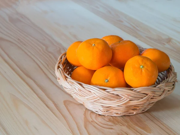 Sinaasappelen op rieten mand, op grenen houten tafel. — Stockfoto