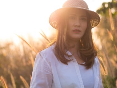 Asyalı güzel kadın çayırda, beyaz gömlek giymiş ve kahverengi şapka giyiyor. Güneşli günlerde.