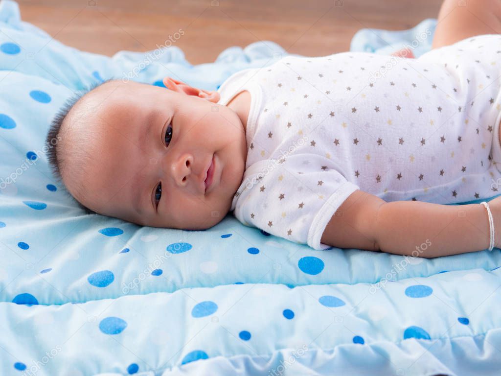 close up, asian newborn baby smiling on cerulean color mattress .