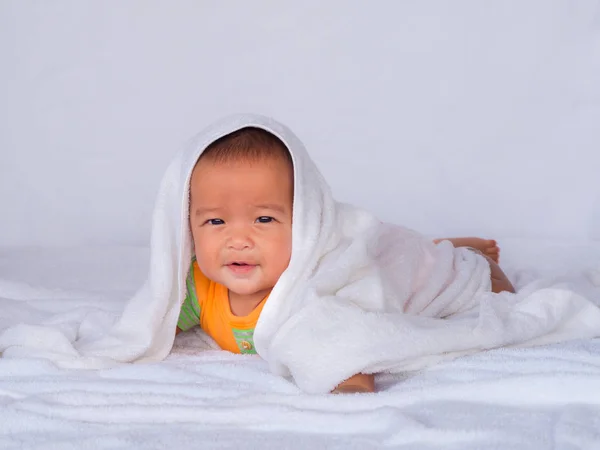 Bebé asiático acostado en el estómago, usando una camisa naranja en un paño blanco. bajo una toalla blanca . — Foto de Stock