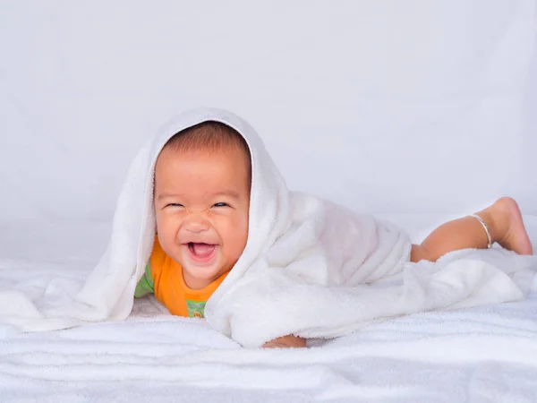 Bebé asiático acostado en el estómago, usando una camisa naranja en un paño blanco. bajo una toalla blanca . — Foto de Stock