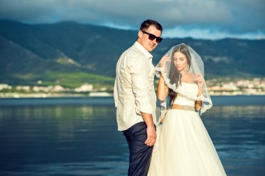 Genç sadece evli çift gelinlik ve takım elbise arka plan üzerinde Dağları ile deniz kenarında.