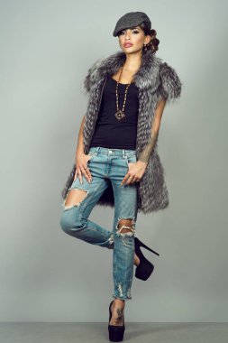 Güzel bir glam portresi kışkırtıcı makyaj giyen gümüş tilki ceket, kot, yüksek topuklu ayakkabılar ve bitkin kap sökük modeliyle dövme