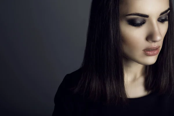 Portrait of gorgeous dark-haired woman with provocative make up looking down with sad expression on her face. — Stock Photo, Image