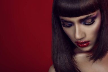 Parlak renkli kışkırtıcı makyaj, pürüzsüz parlak esmer ve çıplak omuz aşağı bakıyor güzel kız portresi. Kırmızı zemin üzerine izole