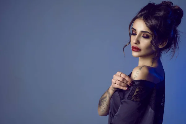 Gyönyörű szexi sötét hajú tetovált fiatal nő vesz egy fekete selyem peignoir, ki vállán csábítóan provokatív make-up és fejtetőre fésült frizura haj portréja — Stock Fotó