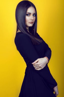 Portre profesyonel makyaj ve uzun kollu ile siyah elbise giyen ve kuşkuyla bakan uzun düz parlak saçlar ile genç güzel esmer