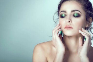 Mükemmel deri ve parlak makyaj yüzünü manikürlü parmaklarıyla dokunarak ile genç güzel kadın portresi. Beyaz arka plan üzerinde izole