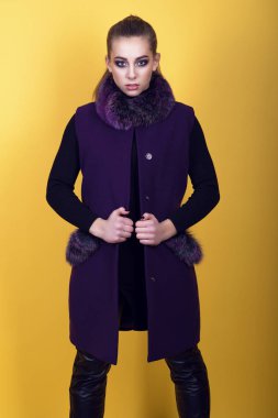 At kuyruğu ve sanatsal makyaj giyen siyah deri pantolon ve trendy mor kolsuz ceket kürk yaka ve cepler, onun Ayaklarınızı omuz genişliği ayrı genç güzel model portresi