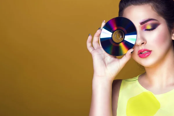 Portrait of young pretty girl with colourful artistic make-up and updo hair holding a CD in front of her eye, enjoyment on her face — Stock Photo, Image