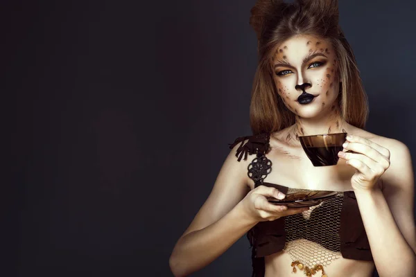Retrato de la joven hermosa modelo de ojos azules con maquillaje artístico de leopardo y pelo cepillado mirando directamente a la cámara y tomando café . — Foto de Stock