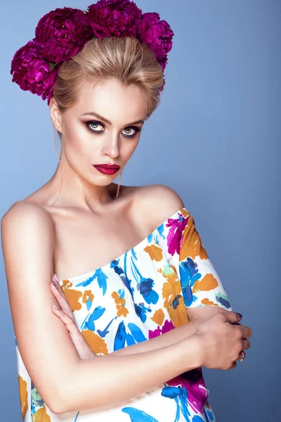 Portret piękny model blond fryzury updo i doskonałe jasne tworzą sobie kolorowy otwarte ramiona sukienkę z kwiatowy wydruku i piwonia Girlanda z głowy, stojąc z rękami skrzyżowanymi — Zdjęcie stockowe