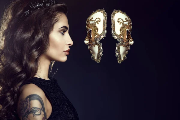 Крупним планом портрет чарівною леді з темно хвилясте волосся шовковистою і ідеальний макіяж, носіння коштовності корони і дивлячись в умовах венеціанських маски, що висять у повітрі — стокове фото