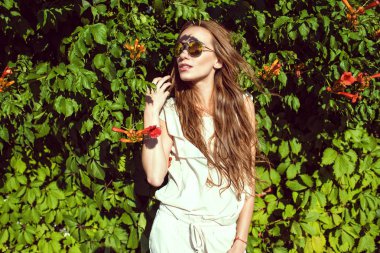 Genç güzel kadın uzun kestane saç çiçeği kokulu asması hedge ayakta trendy yuvarlak yansıtılmış güneş gözlüğü takıyor Rüzgar tarafından üflenir ile
