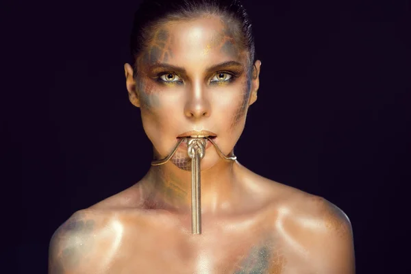 Retrato de cerca de una hermosa mujer con ojos amarillos, piel de serpiente artística maquillaje y cabello liso con lujoso collar de oro en la boca . — Foto de Stock