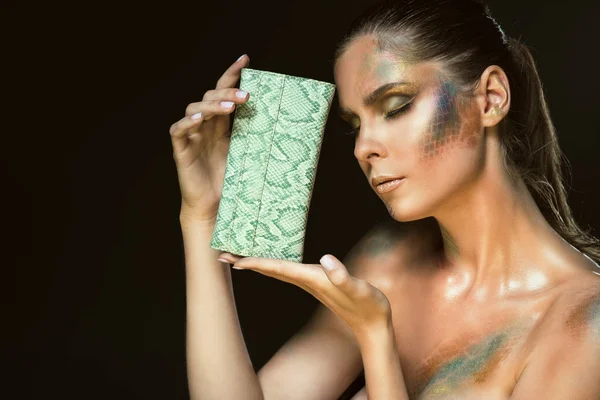 Primer plano retrato de una mujer hermosa con los ojos cerrados y piel de serpiente artística conforman la celebración de bolso de cuero verde en su cara — Foto de Stock