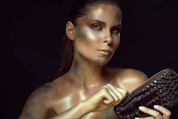 Gros plan portrait de magnifique femme aux yeux jaunes et la peau de serpent artistique maquillage tenant le cuir verni brun foncé zip autour du sac à main et le dézippant — Photo