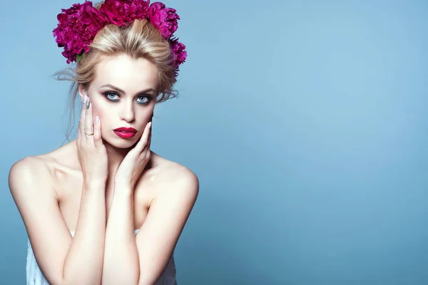 Retrato de la hermosa modelo rubia con el pelo updo soplado por el viento y maquillaje perfecto con peonía guirnalda cabeza sosteniendo sus manos en su cara — Foto de Stock