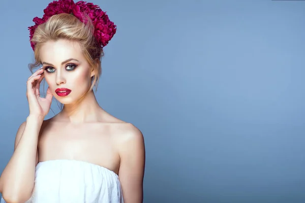 Retrato de belo modelo loiro com cabelo updo e maquiagem perfeita vestindo peônia cabeça guirlanda tocando seu rosto com a mão . — Fotografia de Stock