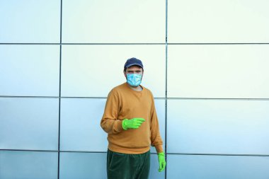 Tıbbi maskeli ve eldivenli adam dışarıda.