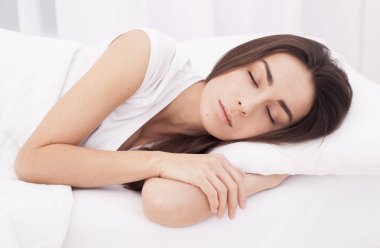 Güzel, genç, esmer kadın beyaz bir yatakta uyuyor..