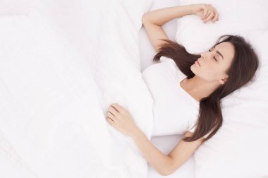 Güzel, genç, esmer kadın beyaz bir yatakta uyuyor..