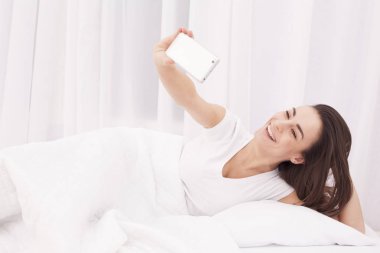 Çok güzel bir genç esmer kız selfie bir beyaz yatakta yapıyor.