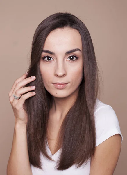 Porträt einer eleganten jungen brünetten Frau in einem weißen T-Shirt, die in die Kamera blickt und ihre Haare streicht. — Stockfoto