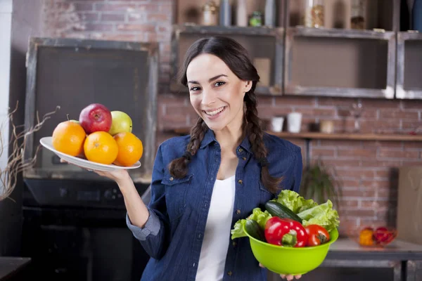 Jonge vrouw in de keuken. Gezonde voeding. Dieet Concept. Gezonde levensstijl. Thuis koken. Eten bereiden. Zeer mooie vrolijke jonge brunette vrouw houden van groenten en fruit en glimlachen. — Stockfoto