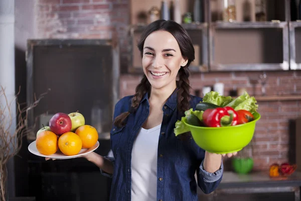 Jonge vrouw in de keuken. Gezonde voeding. Dieet Concept. Gezonde levensstijl. Thuis koken. Eten bereiden. Zeer mooie vrolijke jonge brunette vrouw houden van groenten en fruit en glimlachen. — Stockfoto