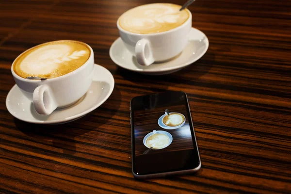 Чашки капучино и смартфон — стоковое фото