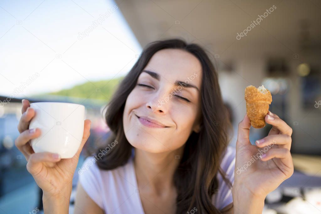 woman eating croissant and drinking coffee