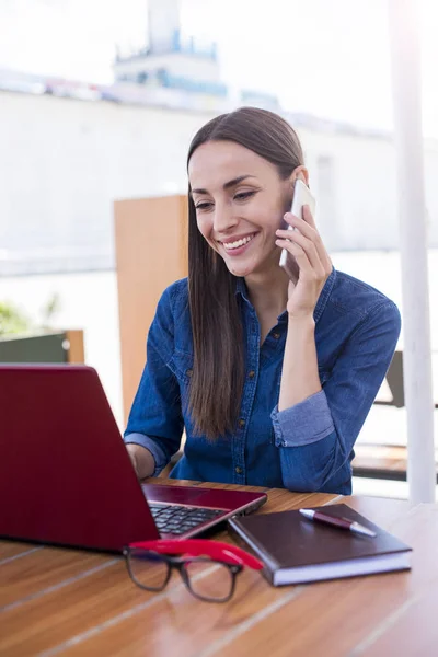 Mujer escribiendo en el ordenador portátil y hablando en el teléfono inteligente — Foto de Stock