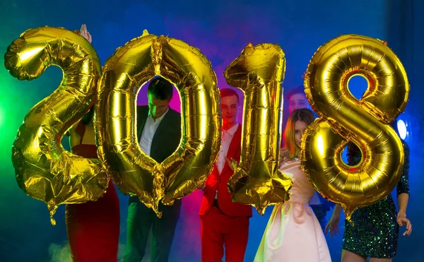 The composition of the golden balloons in the form of figures on a background of a dancing group of young people. The new year 2018. Festive New Year party or disco.