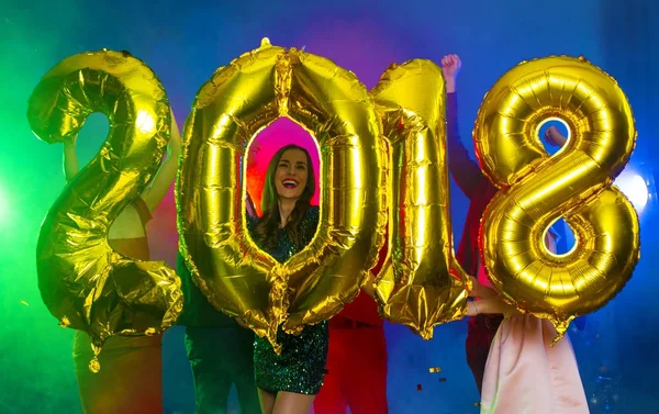 The composition of the golden balloons in the form of figures on a background of a dancing group of young people. The new year 2018. Festive New Year party or disco.