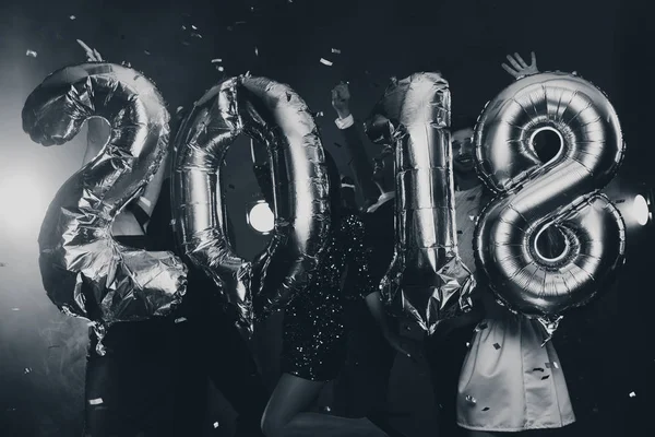 The composition of the golden balloons in the form of figures on a background of a dancing group of young people. The new year 2018. Festive New Year party or disco. Black and white photo