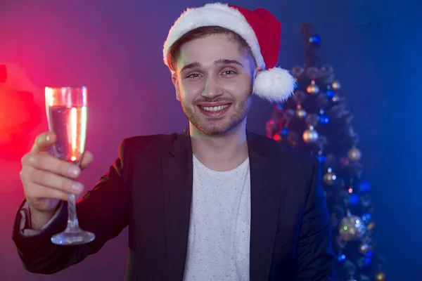 良い新年 そしてメリー クリスマス新年のツリーの背景にシャンパン グラスでサンタ クロースの帽子のハンサムな笑顔若いビジネス人 オフィスの企業 — ストック写真