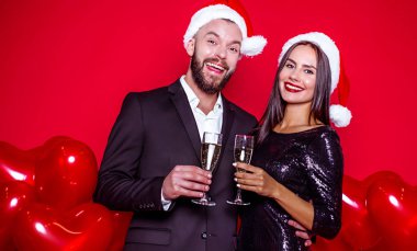 Bir güzel yeni yıl ve Noel var. Neşeli güzel gülümseyen birkaç bardak şampanya topları ile kırmızı bir arka plan ile Noel Baba şapkaları severler. Tatil severler
