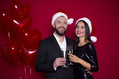Bir güzel yeni yıl ve Noel var. Neşeli güzel gülümseyen birkaç bardak şampanya topları ile kırmızı bir arka plan ile Noel Baba şapkaları severler. Tatil severler